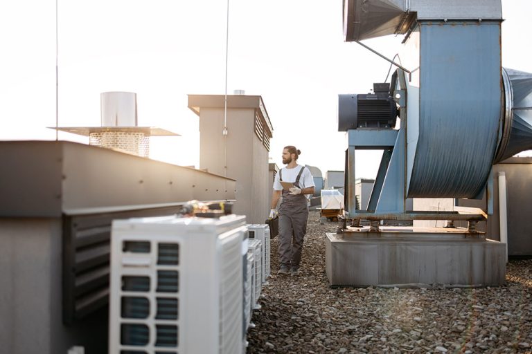 HVAC technician carrying a tool case and tablet while inspecting commercial rooftop air conditioning and ventilation units.