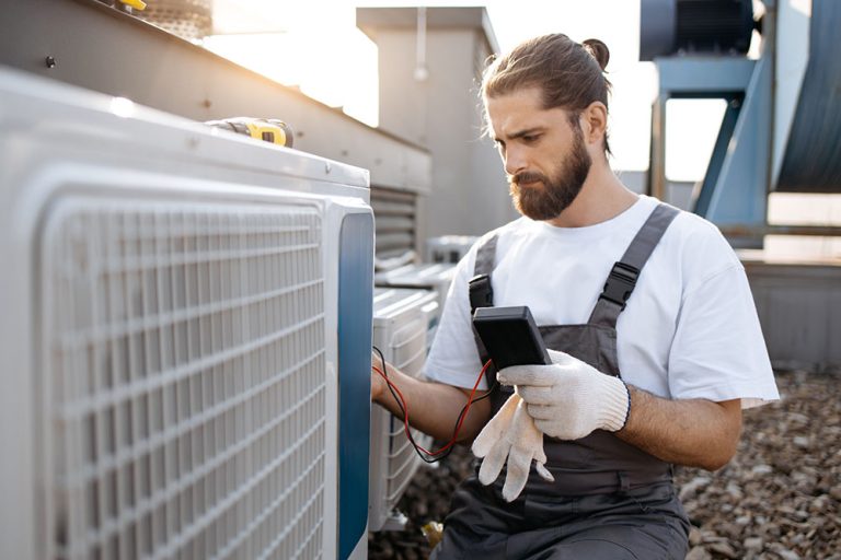 Professional HVAC technician using a digital multimeter to test electrical output on a rooftop air conditioning condenser unit.